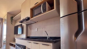 A modern kitchen with built-in appliances, a flat-screen TV, and a stainless steel refrigerator. - Studio c/ Varanda Vista Mar • Stella Maris & Farol (Salvador)