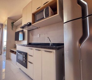 A modern kitchen with built-in appliances, a flat-screen TV, and a stainless steel refrigerator. - Studio c/ Varanda Vista Mar • Stella Maris & Farol (Salvador)