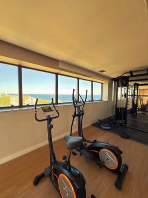 A gym with two exercise bikes, a weight bench, and a mirror. - Studio c/ Varanda Vista Mar • Stella Maris & Farol (Salvador)