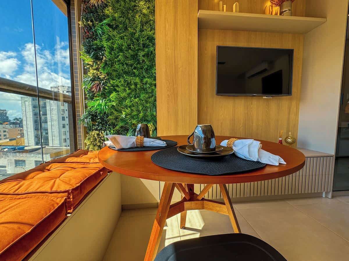 A modern dining area with a round table, a television mounted on the wall, and a view of the city through large windows.