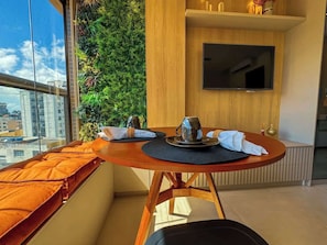 Un espace repas moderne avec une table ronde, un téléviseur fixé au mur et une vue sur la ville grâce à de grandes fenêtres.