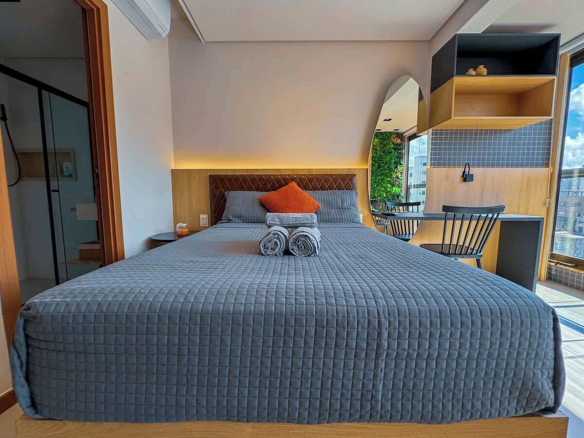 A hotel room with a large bed, a nightstand, a chair, and a view of the city through the window.