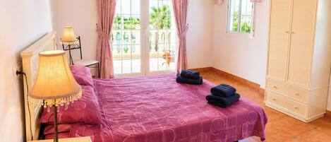 Un dormitorio con cama, mesita de noche, lámpara, armario y vista al exterior.