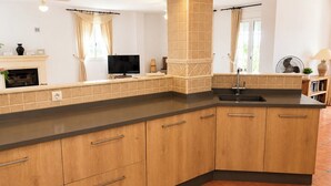 A kitchen with wooden cabinets, a black countertop, a sink, a television, and a window with curtains. - Villa La Vida Antas by Ruralidays (Almería)