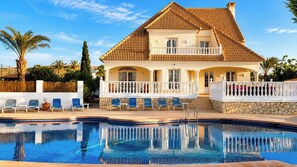 Ein zweigeschossiges Haus mit Swimmingpool, einem Balkon mit Stühlen und einer Steinsäule.