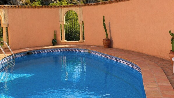 A swimming pool with a geometric tile pattern, a small arched window, and potted cacti.