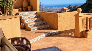 A terrace with steps leading to a balcony, outdoor furniture, and a view of the landscape.