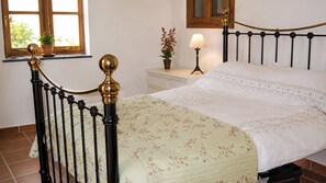 A bedroom with a bed, a nightstand, a lamp, and a window with a view of greenery.