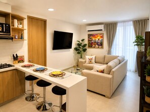 Ein modernes Wohnzimmer mit Küchenzeile, einem Esstisch mit Barhocker, einer Couch und einem flachbildfernseher an der Wand.
