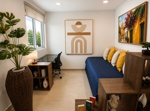 A modern bedroom with a desk, a large potted plant, a bed with colorful pillows, and a painting on the wall. -   Luxury Beach Apartment, Master Suite + Office, Walk to the Beach (Cartagena)