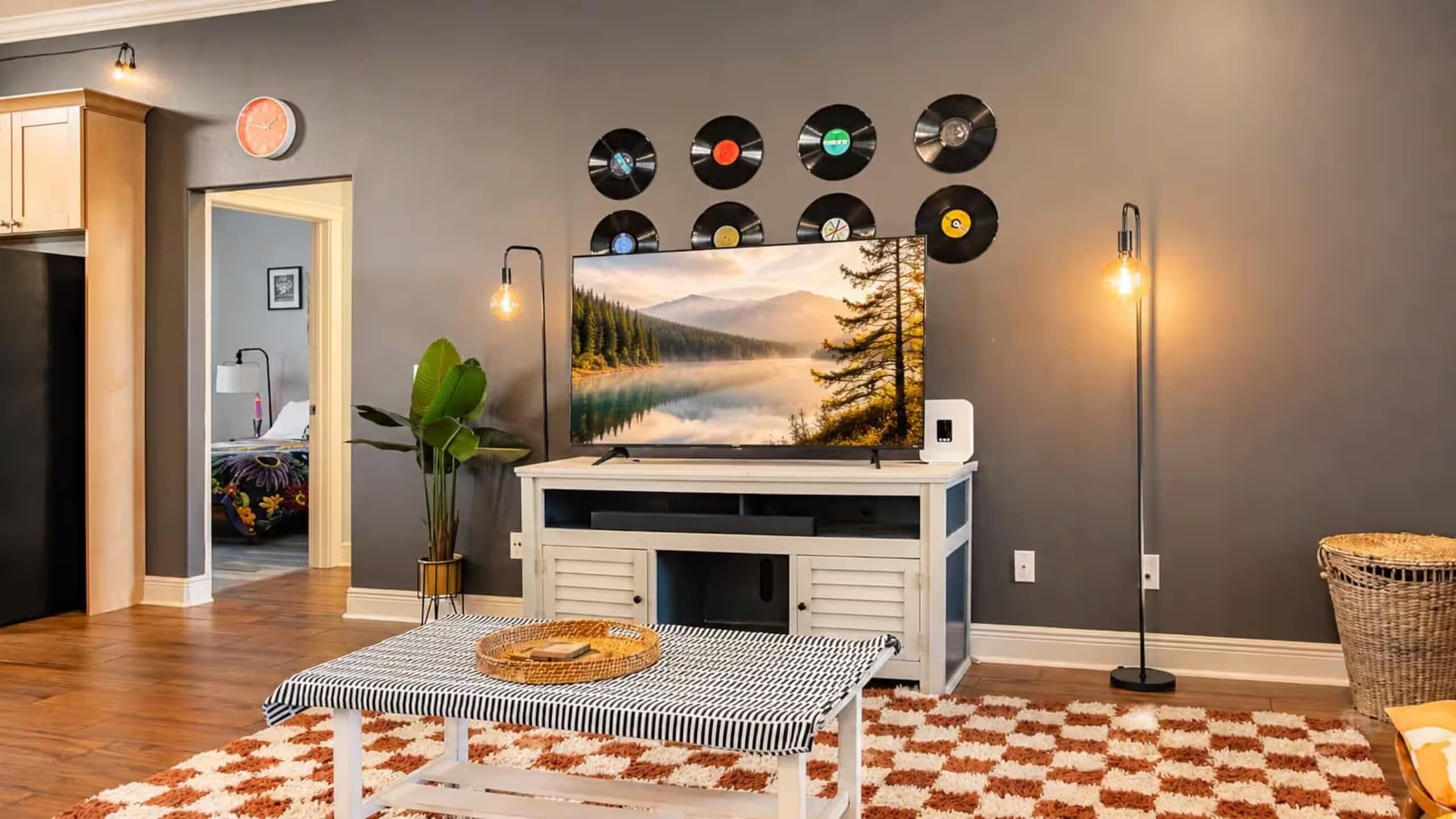 A living room with a fireplace, a painting of a lake, and a collection of vinyl records on the wall.