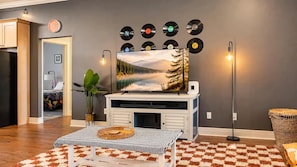 A living room with a fireplace, a painting of a lake, and a collection of vinyl records on the wall.