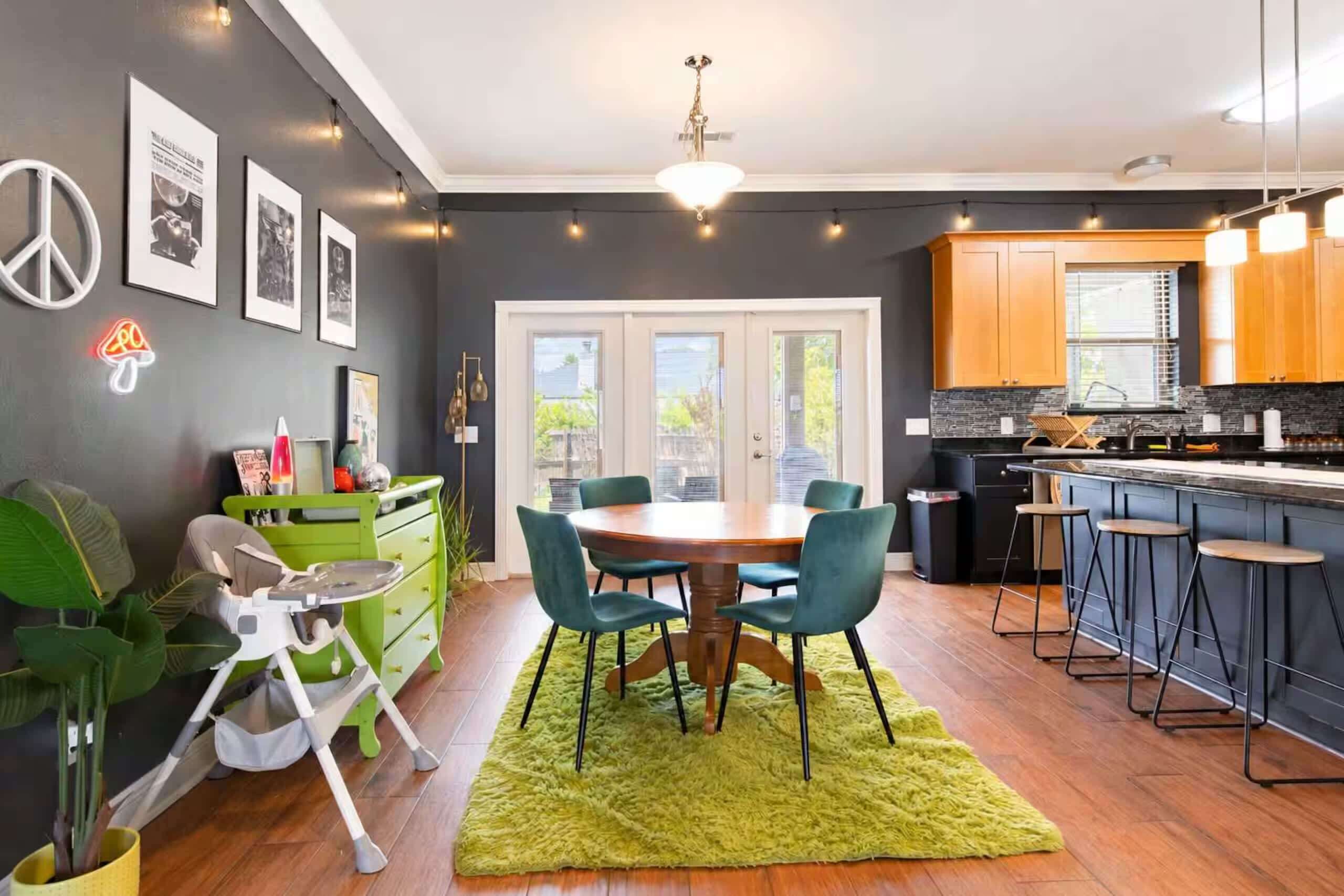 Une cuisine moderne avec un coin repas, comprenant une table verte, des chaises turquoise et un bar avec des tabourets.