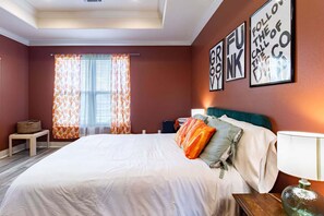 Un dormitorio con cama, almohadas, una mesita de noche, lámpara y ventana con cortinas.