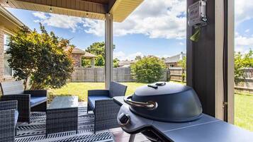 Un patio exterior con una parrilla, mobiliario de mimbre y un área techada.