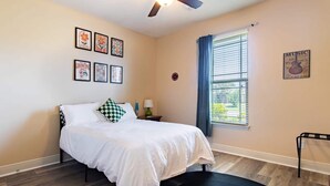 Un dormitorio con cama, ventana con persianas, ventilador de techo y decoración en las paredes.