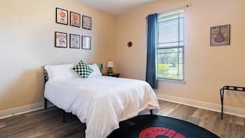 Un dormitorio con cama, ventana con persianas, ventilador de techo y decoración en las paredes.