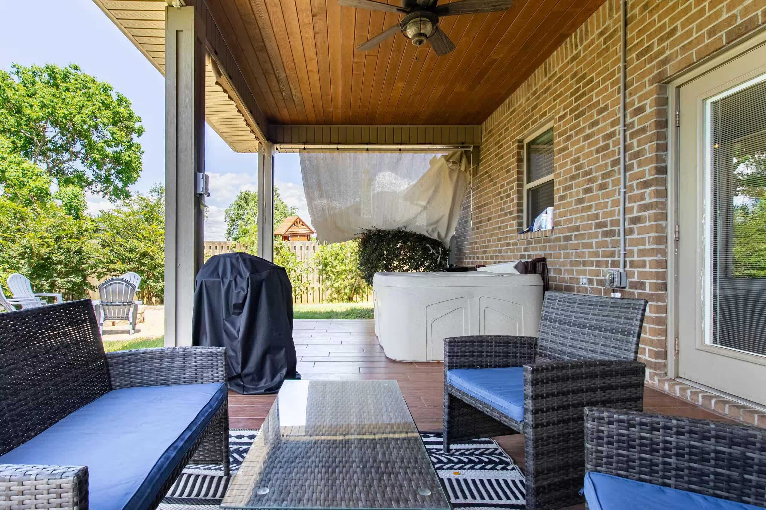 A covered patio with outdoor furniture, a barbecue grill, and a hot tub.