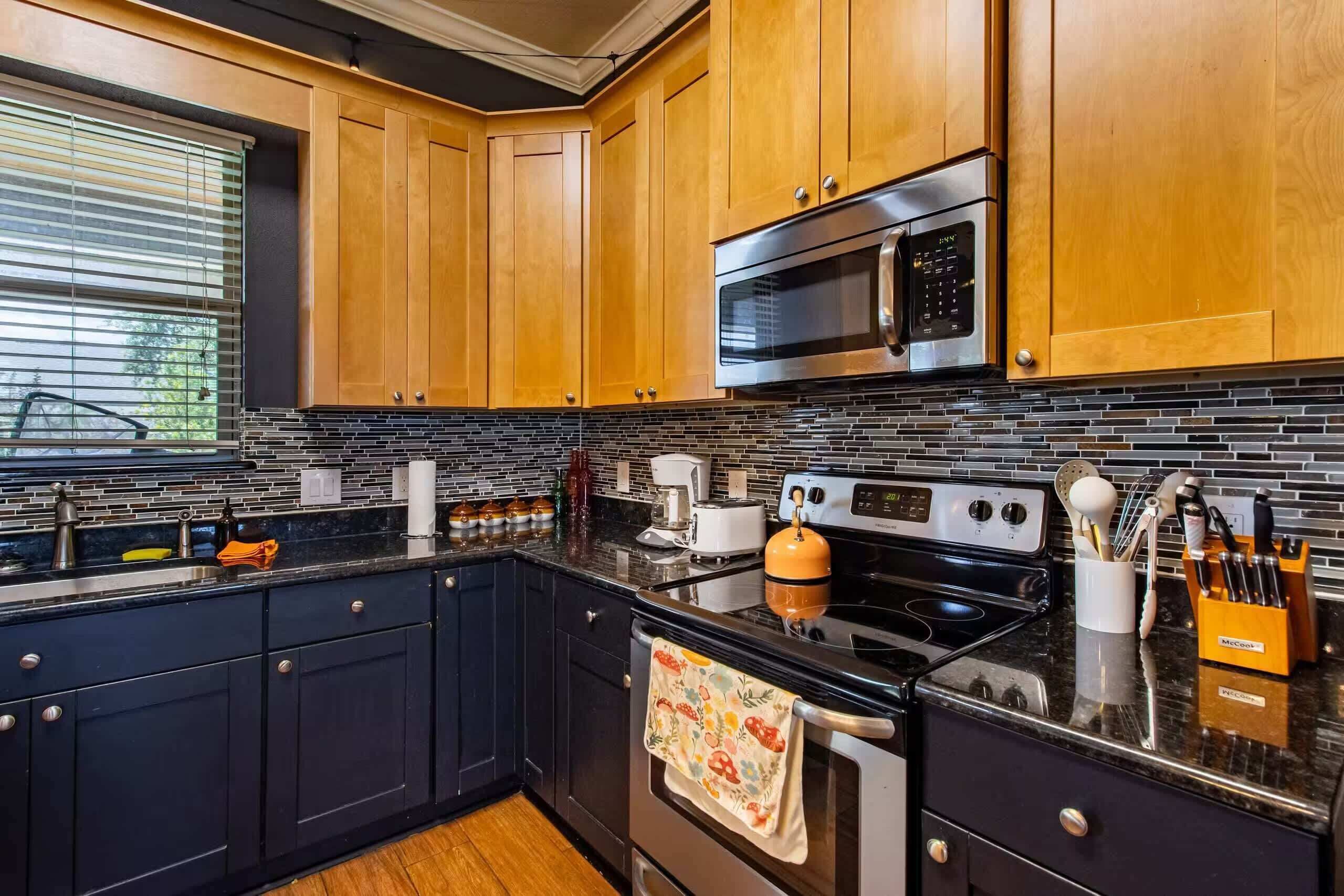 A modern kitchen with dark cabinetry, a stainless steel microwave, a gas stove, and a black countertop.