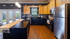 Una cocina moderna con una isla central, armarios negros, electrodomésticos de acero inoxidable y suelo de madera.