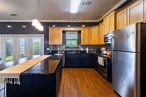 A modern kitchen with a central island, black cabinetry, stainless steel appliances, and a wooden floor. - Gulf Breeze Oasis: Hot Tub, Pet-Friendly, Beach (Gulf Breeze)