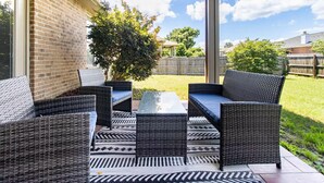 Un patio al aire libre con mobiliario de mimbre y una mesa de vidrio.