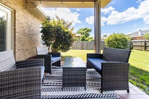 An outdoor patio with wicker furniture and a glass table. - Gulf Breeze Oasis: Hot Tub, Pet-Friendly, Beach (Gulf Breeze)