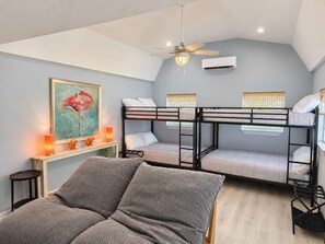 A room with bunk beds, a ceiling fan, an air conditioning unit, a painting, and a bedside table with a lamp. - Navarre Beach Retreat | Hot Tub & Teen Bunkhouse (Navarre)