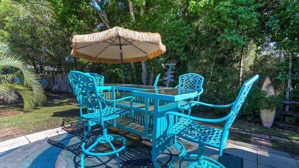 A patio with a table and chairs, surrounded by greenery. - Navarre Oasis: Tiki Bar, Hot Tub, Near Beach (Navarre)
