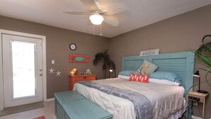 A bedroom with a bed, a nightstand, a desk, a ceiling fan, a clock, and a door. - Navarre Oasis: Tiki Bar, Hot Tub, Near Beach (Navarre)