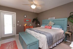 Ein Schlafzimmer mit einem Bett, einem Nachttisch, einem Schreibtisch, einem Deckenventilator, einer Uhr und einer Tür.