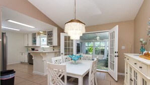A spacious kitchen with white cabinetry, a dining area with a white table and chairs, and a chandelier. - Navarre Oasis: Tiki Bar, Hot Tub, Near Beach (Navarre)