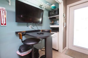 A room with a flat-screen TV mounted on the wall, a small round table with two chairs, and a door with a doormat. - Navarre Beach Retreat | Hot Tub & Teen Bunkhouse (Navarre)