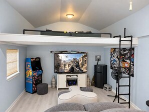 A loft-style room with a TV, gaming console, and a ladder. - Navarre Beach Retreat | Hot Tub & Teen Bunkhouse (Navarre)