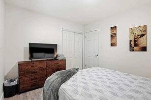 A bedroom with a bed, a dresser, a television, and two doors. - Indy 3BR | Game Room + Fire Pit | Sleeps 8 (Indianapolis)