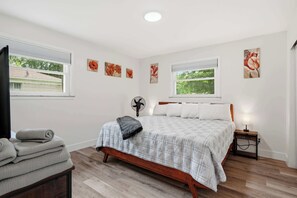 A bedroom with a bed, a bedside table with a lamp, a fan, and artwork on the walls. - Firepit & Gameroom Retreat in Devon Hills (Indianapolis)