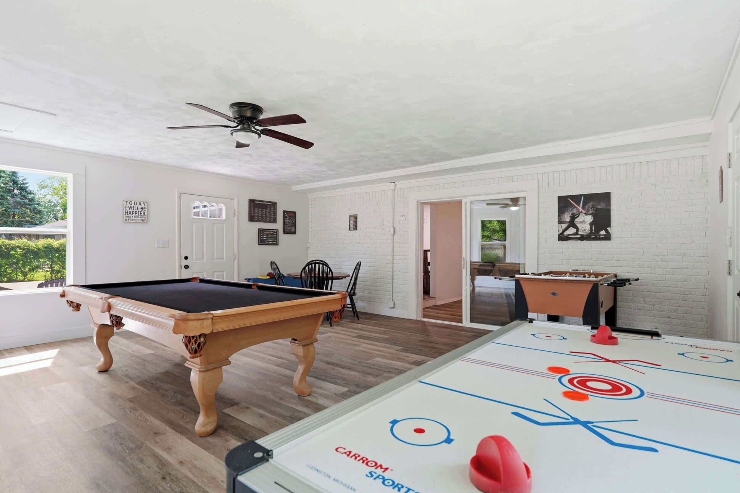 Um quarto com mesa de bilhar, mesa de pebolim e ventoinha no teto.