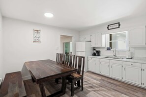 A modern kitchen with white cabinetry, a wooden dining table, and a sign that reads 'Market Fresh.' - Firepit & Gameroom Retreat in Devon Hills (Indianapolis)