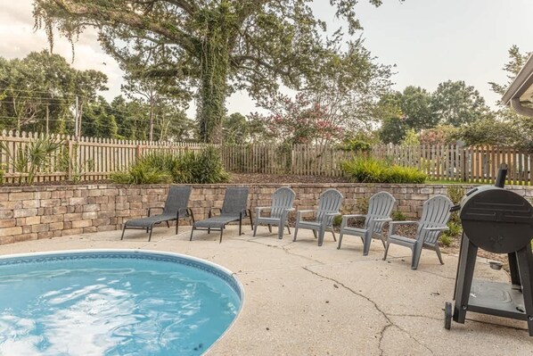 A swimming pool with lounge chairs and a barbecue grill.
