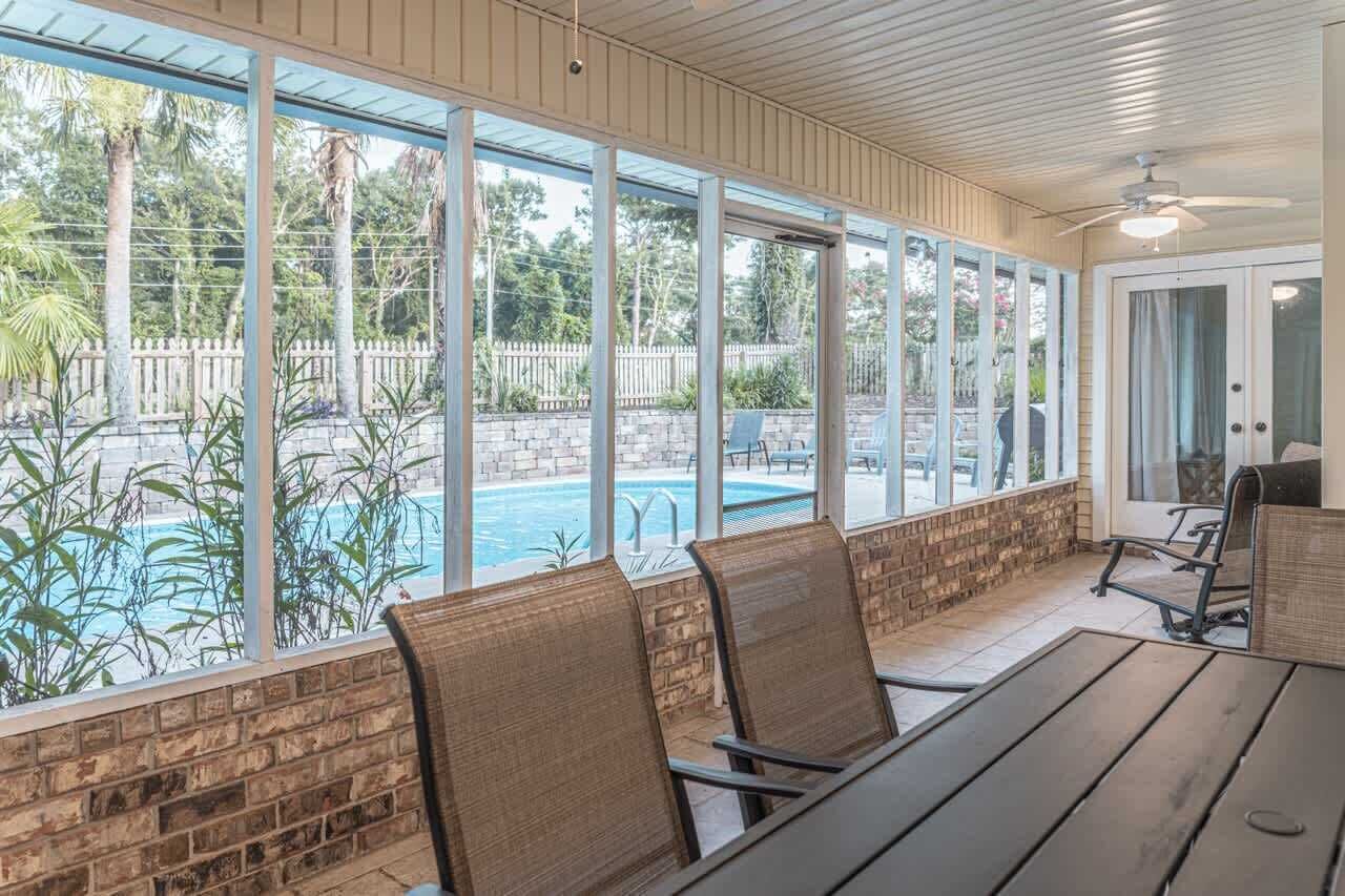 A covered outdoor seating area with a view of a swimming pool and a brick wall.