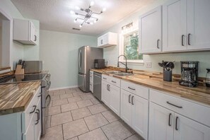 A kitchen with white cabinets, a stainless steel refrigerator, a coffee maker, and a window with a view of trees. - Private Pool | 3BR/3BA | Near Pensacola Beach (Pensacola)