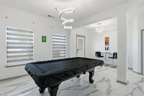 Une pièce comprenant une table de billard, une porte et un coin salon avec deux fauteuils et une table.