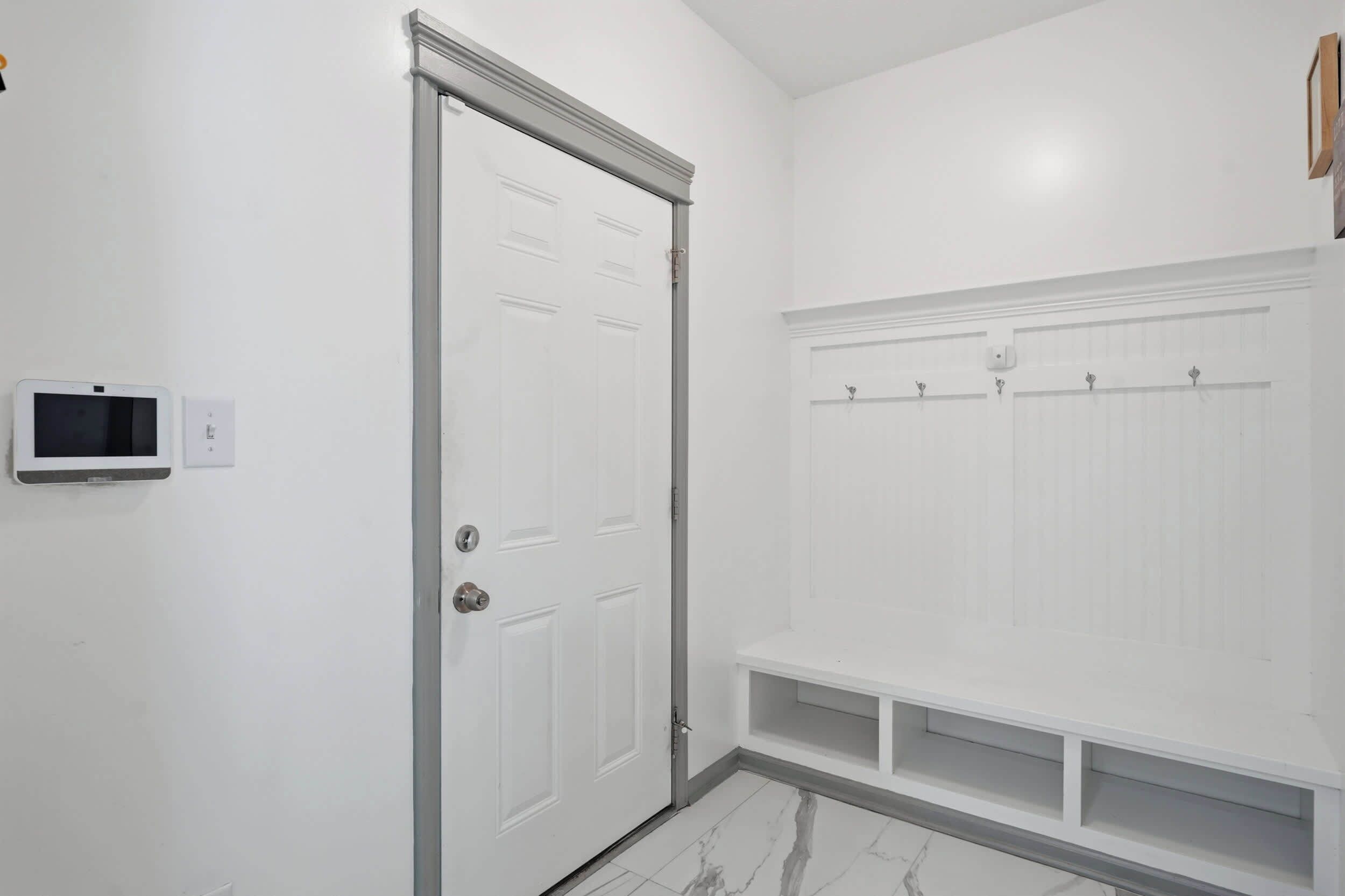 Un baño limpio y blanco con puerta, zona de ducha y suelo de baldosas.