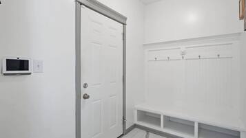 Un baño limpio y blanco con puerta, zona de ducha y suelo de baldosas.