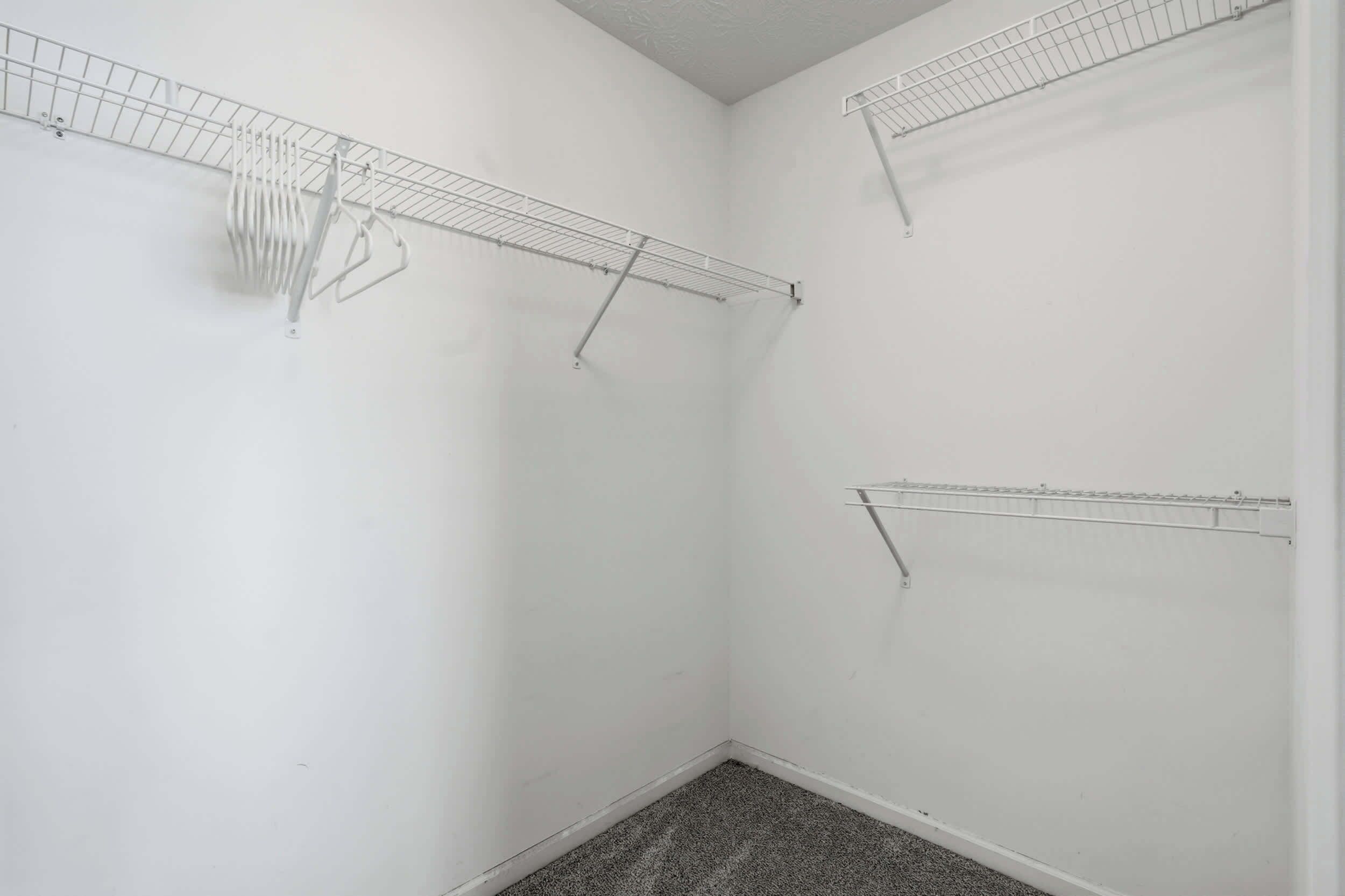 Una habitación con paredes blancas, alfombra gris y tres tendederos metálicos.