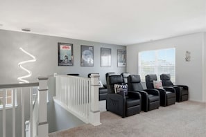 Une salle de cinéma maison avec une rambarde blanche, des fauteuils inclinables en cuir noir et des affiches de films accrochées au mur.