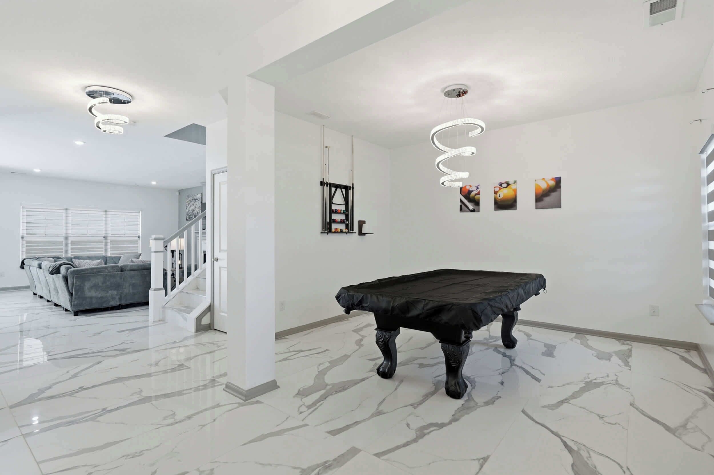 Una habitación amplia con mesa de billar, un sofá y una escalera que lleva a otra zona.