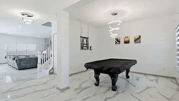 Una habitación amplia con mesa de billar, un sofá y una escalera que lleva a otra zona.