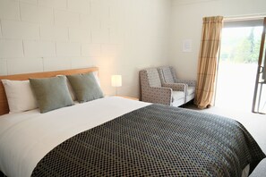 A hotel room with a bed, a chair, a patterned bedspread, and a window with curtains. - Mora Motels (Wānaka)