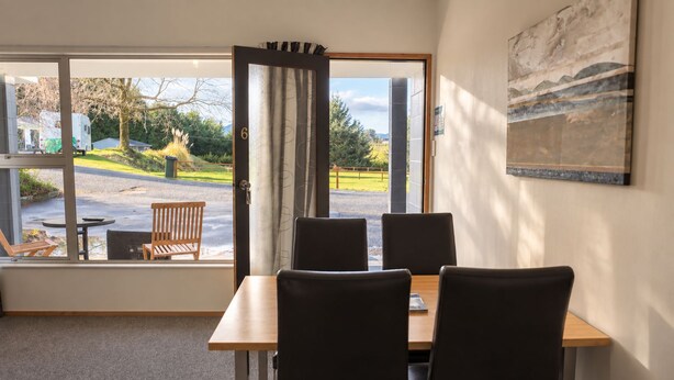 A room with a table and chairs, a window with a view of the outside, and a painting on the wall. - Sundale Mora Motels (Wānaka)